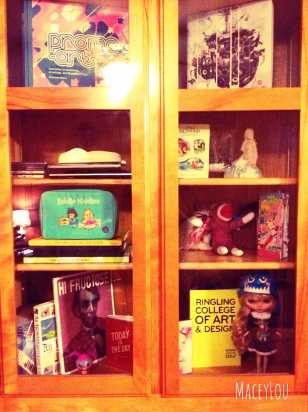 cabinet full of cute things such as a little kiddles lunch box filled with crayons, a blythe doll with big eyes, and pretty books